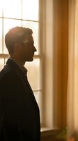 Thoughtful businessman in profile gazing through office window with warm sunlight streaming in, creating contemplative atmosphere for corporate concepts.