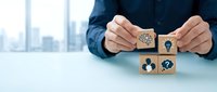 Business professional arranging wooden blocks with innovation icons including gears, lightbulb, and teamwork symbols on modern office desk for strategy planning.