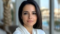 Professional young Hispanic businesswoman in white blazer smiling confidently at camera in modern office environment for corporate headshot and business portrait.