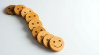 Wooden smiley face tokens arranged in curved line on white background. Natural wood circles with happy expressions for crafts and educational activities.