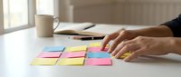 Hands arranging colorful sticky notes on a white desk in a bright office, organizing tasks and ideas for productivity and planning.
