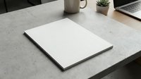 Blank white notebook or sketchbook lying open on modern workspace desk with laptop, coffee mug and small plant in background for creative projects.