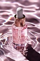 Pink glass dropper bottle with rose gold cap on rippled water surface reflecting soft light, luxury skincare serum product photography for cosmetic advertising.