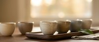 Handmade ceramic bowls and cups arranged on wooden tray with soft natural lighting for kitchen dining and home decor styling.