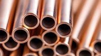 Copper pipes and tubes in industrial setting showing circular ends with metallic shine and reflective surface. Close up view creates abstract pattern.