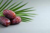 Fresh medjool dates arranged on palm leaf against light background, healthy natural dried fruit closeup with copy space for Ramadan season.