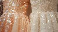 Elegant wedding dresses with delicate pearl embellishments and sparkly details in beige and ivory tones, close-up view showing luxurious fabric texture and intricate beadwork.