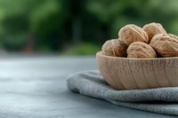 Fresh walnuts in wooden bowl on gray linen napkin with blurred green garden background for healthy eating and natural nutrition concepts.