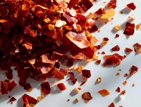 Red chili pepper flakes scattered on white background, spicy seasoning ingredient for cooking and food preparation.