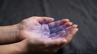 Young adult with medium skin tone holding glowing purple holographic data visualization in open palm against dark background, representing technology, digital innovation, and future computing concepts.