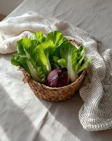 Fresh green lettuce and purple cabbage in woven basket on light linen tablecloth with textured cloth, natural food styling for healthy eating concept.
