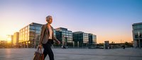 Middle-aged Caucasian male professional in business attire carrying leather briefcase walking across modern urban plaza at sunset, suitable for corporate, finance, and business lifestyle content.
