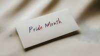 Handwritten text Pride Month in rainbow colors on white paper note against blurred neutral background, celebrating LGBTQ+ community and diversity.
