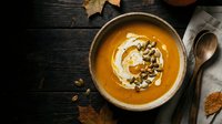 Creamy pumpkin soup with swirl of cream and toasted seeds in rustic bowl on dark wooden table. Autumn comfort food ready for seasonal dining and cozy meals.