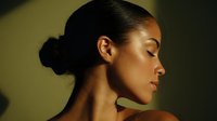 Young African American woman with closed eyes in profile against dark background, illuminated by warm dramatic lighting creating strong shadows and highlighting facial features.