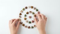Female hands arranging colorful gemstone hearts in spiral pattern on white background for healing crystal therapy and meditation practice.