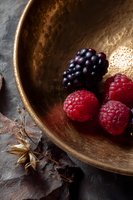 Fresh ripe raspberries and blackberry in vintage bronze bowl on dark stone background with star anise spice, moody food photography composition.