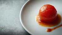 Elegant roasted red tomato with caramelized sauce on white ceramic plate, gourmet fine dining presentation for culinary arts and restaurant menu design.