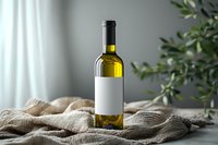 Wine bottle with blank white label on natural linen tablecloth against soft gray background with olive tree branch, minimalist product photography setup.