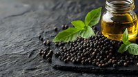 Fresh black peppercorns scattered on dark stone surface with glass jar of olive oil and green basil leaves, moody food photography with copy space.