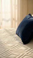 Cozy bedroom scene with navy blue pillow resting on quilted cream bedding near sunlit window with sheer curtains, ideal for home decor and lifestyle design projects.