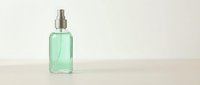 Green glass spray bottle with silver pump dispenser on neutral background for cosmetic and skincare product mockups.