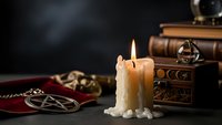 Mystical candle flame illuminates occult symbols, antique wooden chest and brass compass on dark surface creating atmospheric witchcraft scene for spiritual content.