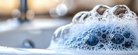 White soap foam bubbles with blue reflections on blurred background creating abstract macro photography composition. Suitable for cleaning and hygiene concepts.