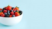 Fresh mixed berries including strawberries, blueberries, and blackberries in white bowl on light blue background for healthy eating and nutrition content.