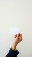 Female hand holding blank white card against neutral background, wearing gold ring and bracelet. Isolated on light beige backdrop for mockup and branding design use.