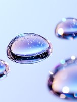 Macro photography of water drops with purple and blue gradient reflections creating abstract shapes on light background, artistic close-up with bokeh effect.