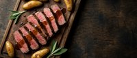Sliced grilled beef steak with roasted potatoes and herbs on wooden cutting board, perfect for restaurant menus and culinary presentations.