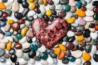 Red heart-shaped stone surrounded by colorful polished gemstones and pebbles on white background. Love, romance, healing crystals concept.