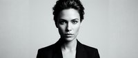 Professional businesswoman in black blazer with confident expression and modern hairstyle against neutral background for corporate branding.