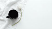 Black coffee mug on white linen cloth with a white tulip flower, minimalist flat lay composition with copy space.