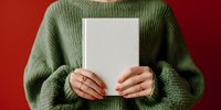 Woman in green sweater holding blank white book against red background, perfect for book cover mockup or publishing concept.