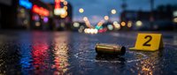 Crime scene investigation with bullet casing and evidence marker on wet asphalt street at night with police lights and urban bokeh background.