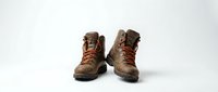Pair of worn brown leather hiking boots with laces and rugged soles, isolated on white background for outdoor adventure, trekking, and mountaineering projects.