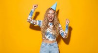 Young blonde woman celebrating birthday with party hat dancing joyfully on bright yellow background for festive occasions and party invitations.