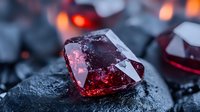 Red translucent crystal on dark stone surface with glowing backlight creating mysterious atmosphere, macro photography showing facets and reflections in gemstone.