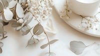 Delicate white baby's breath flowers and silver eucalyptus leaves arranged with ceramic cup on white background, creating soft romantic wedding styling composition.
