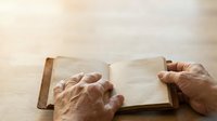 Elderly hands with wrinkled skin opening blank pages of aged book on wooden surface, symbolizing wisdom, knowledge, reading, and life experience for educational and inspirational content.