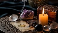 Mystical fortune telling setup with tarot cards, burning candle, amethyst crystals, ornate wooden box and incense smoke creating atmospheric divination scene.