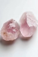 Raw rose quartz crystals with natural rough texture and soft pink hues on white background, mineral specimens showing crystalline structure and healing properties.