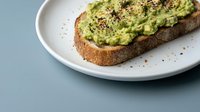 Avocado toast on whole grain bread with seeds and spices on white plate, healthy breakfast meal for social media content and food blogs.