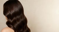 Woman with long wavy brown hair showing healthy shiny locks from behind against neutral background for beauty and haircare concepts.