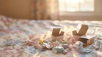 Cozy bedroom scene with fairy lights, scattered papers and craft supplies on floral bedding creating warm artistic atmosphere for creative projects.