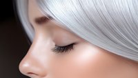Close up profile view of young Asian woman with silver gray hair and long eyelashes against dark background, eyes closed in serene expression.