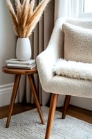 Cozy reading nook with beige armchair, wooden side table, and pampas grass in white vase, creating warm minimalist home decor atmosphere.
