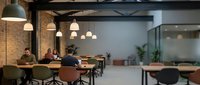 Modern coworking space with exposed brick walls, pendant lighting, and people working at wooden tables in industrial-style office environment.